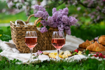 Closeup of two glass of rose wine , picnic basket, croissants, food and flowers on the grass. Banner