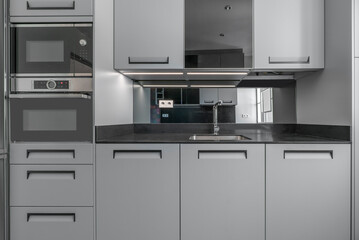 Kitchen front shot with newly installed gray cabinets and drawers with large nails as pulls with black marble counter tops and built-in matching appliances