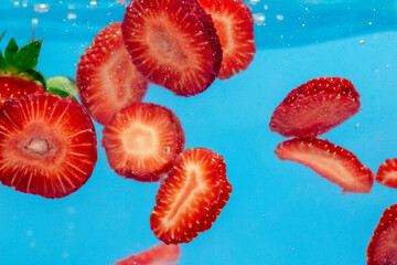 Sliced Strawberry in water with water splash and air bubbles on blue background. Close up image.