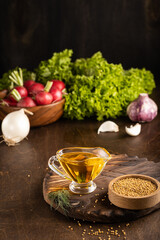 Mustard oil on wooden board background with fresh vegetables. Vertical