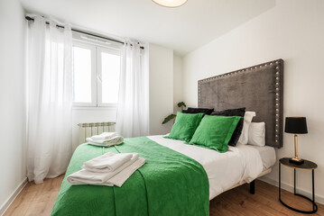 Bedroom with a double bed dressed in a striking green bedspread and matching cushions, upholstered...