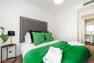 Bedroom with a double bed dressed in a striking green bedspread and matching cushions