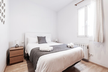 Fototapeta premium Bedroom with double bed, dark wood nightstand with drawers, window with curtains and white duvet