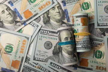 Money, a roll of US hundred dollar bills on a black texture background. Money is scattered on the table. Concepts of finance and economy. Money accumulation concept. Saving currency. Investments.