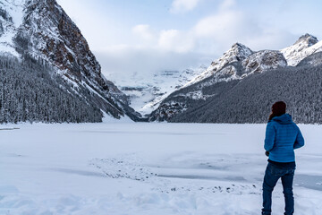 Fototapeta na wymiar Lake Louise, Alberta, Canada - Man tourist standing beside the stunning tourist area in winter time. 