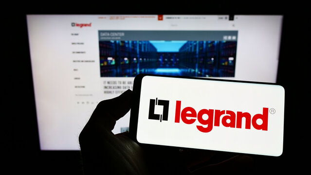 Stuttgart, Germany - 05-21-2022: Person holding smartphone with logo of French electronics company Legrand S.A. on screen in front of website. Focus on phone display.