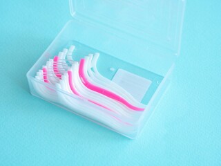 Dental floss with a plastic toothpick in white and pink in a plastic transparent container on blue. Dental concept