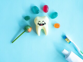 Sweets, lollipops, candies around a crying yellow tooth, toothpaste and brush, space for text....