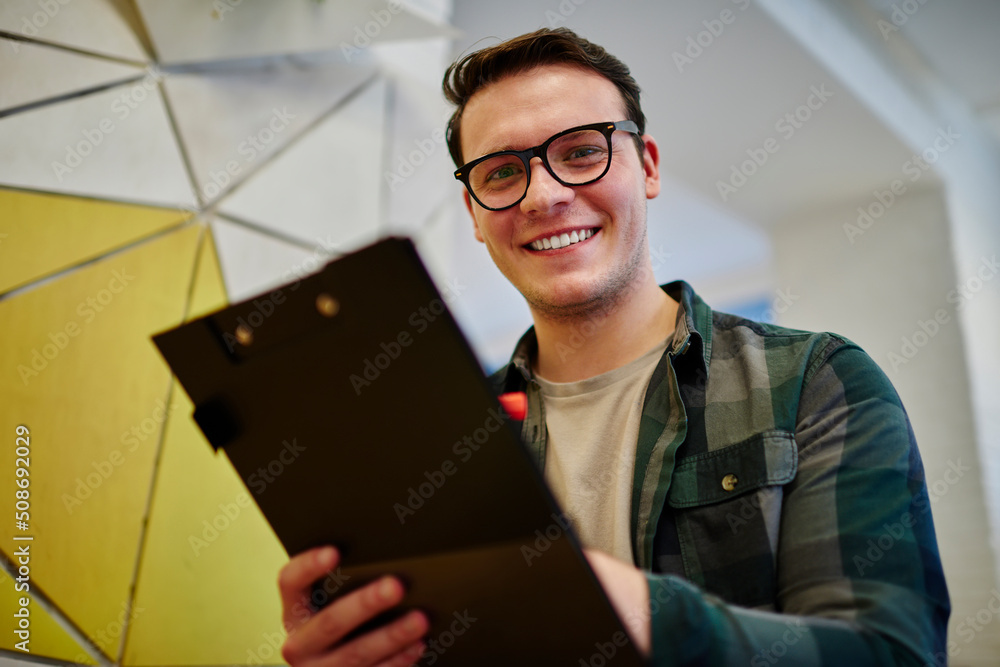 Poster young smiling male student writing notes in notebook while learning. man freelancer work on notebook