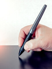 A man holds a pen, a stylus and draws with a graphics tablet