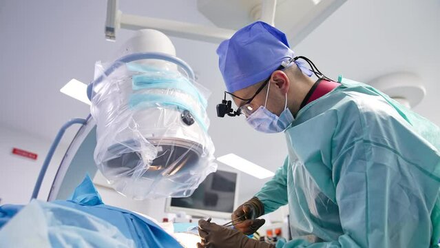 Surgeon stands bent over the patient. Medical specialist uses metal tools to sew the patient.