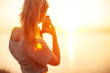 back view of Young woman makes photo on phone  in nature with view and warm light of sunset, makes poses enjoy the meditation, balance and sunrise