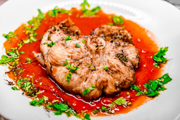 Slice of homemade dogfish dish in red sauce with parsley and herbs in a white plate. Overhead Macro Close-up photography with shallow depth of field, selected focus on the middle of the medallion.