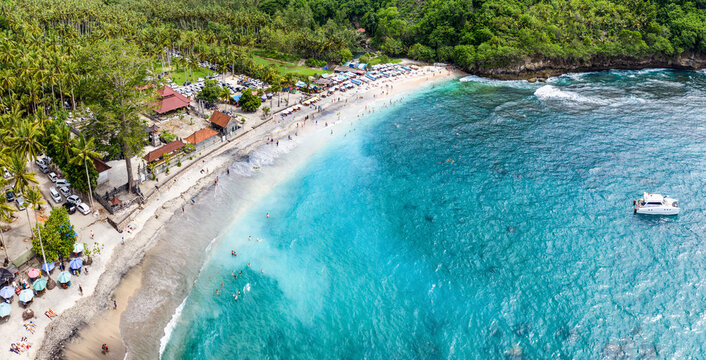 Magnificent aerial panorama up down photo of tropical beach at the end of mountain valley with coconut palms, boats in blue water, unrecognized tourists at Crystal Bay beach, Nusa Penida, Bali