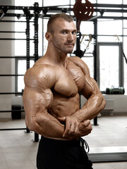 Bodybuilder with perfect physique posing in the gym, demonstrating biceps and pectoral muscles. Muscular man with a naked torso. Classic bodybuilding