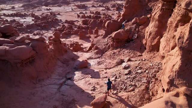 Male hikers walking in red canyon lands desert with cinematic mountain cliffs on the sunrise background. Men exploring wilderness nature. Utah USA
