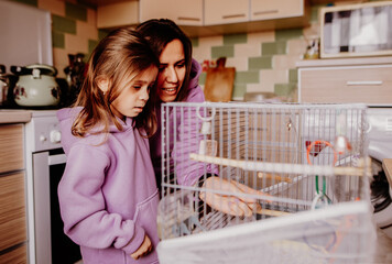 Mother with her daughter standing near cages with parrot at home