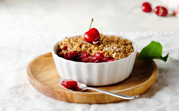 Cramble with cherries in white ceramic bowl on rustic background. Selective focus.