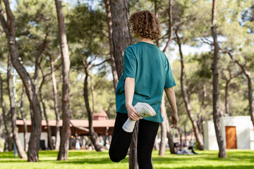 Young caucasian woman wearing green tee standing on city park, outdoor stretching legs before run. Fitness and workout wellness, start straight concept of challenge or career path and change.