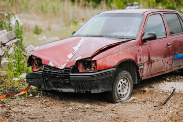 An old, red broken car stands in a landfill after the war in Ukraine in nature.