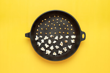 Popcorn in a black pan without a handle, half a pan of corn grains, half of the popcorn. Yellow background. Photography for advertising of cinemas, cafes, restaurants, coffee houses