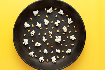 Popcorn in a black frying pan without a handle, randomly mixed corn kernels and popcorn. Yellow background. Photography for advertising cinemas, cafes, restaurants, coffee houses. Horizontal photo.