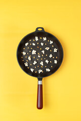 Popcorn in a black pan with a handle, randomly mixed corn kernels and popcorn. Yellow background. Photography for advertising cinemas, cafes, restaurants, coffee houses. Vertical photo.