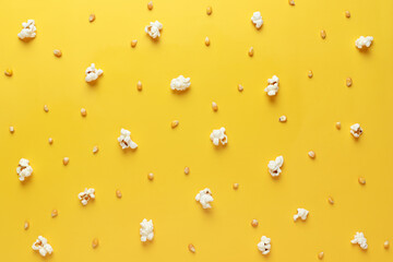 Popcorn and corn kernels are randomly arranged on a yellow background. Photography for advertising cinemas, cafes, restaurants, coffee houses. Horizontal photo.