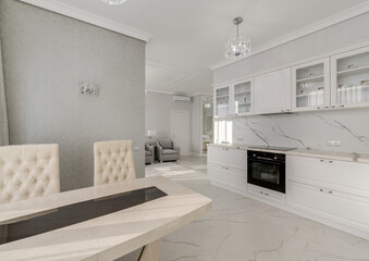 Sunny bright kitchen in classic style in light colors with marble and table