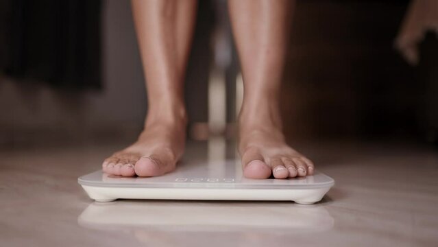 Woman on scales measure weight. girl legs step bathroom scale. Fitness diet woman feet standing weighing. Female dieting checking BMI weight loss. Barefoot measuring body fat overweight. Cinematic 4K