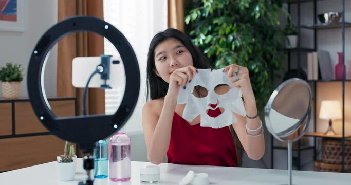 Beauty blogger or vlogger recording product review for brand to share on social media as part of collaboration. Woman holds facial skin care sheet mask in hands tells observers about its benefits.