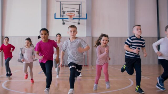 Group of elementary students running during class at school gym.