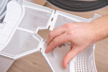 A man takes a lint filter out of the dryer and cleans it from dust, lint, hair, wool.