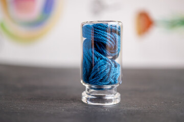 Frasco de vidrio pequeño, al revés, lleno con madeja de hilo de algodón color azul sobre madera...