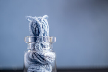 detalle de frasco de vidrio pequeño sobre fondo azul lleno de madeja de hilo de algodón color azul