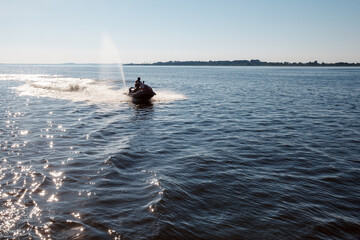 Silhouette of strong man jumps on the jet ski above the water at noon.