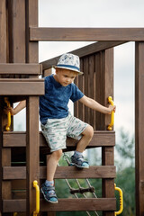 The boy is playing on an outdoor playground, he climbs a wooden ladder dangerously