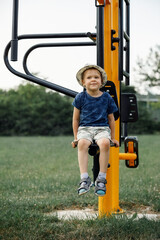 The little boy sitting in on the street exercise machine, child poses to camera. . Active rest with children.
