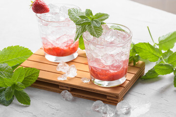 Fresh strawberry mojito cocktail. Two glasses with cold summer strawberry soda drink with strawberry, ice cubes and mint leaves on light grey background. Iced strawberry lemonade, close up