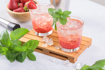 Cold summer strawberry cocktail mojito, margarita, daiquiri. Two glasses with fresh strawberry soda drink with ice cubes and mint leaves on light grey background. Iced strawberry lemonade, close up