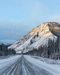 Wilderness road, highway in northern Canada with mountains towering over the below wilderness. Road...