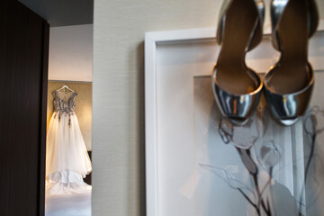 Wedding dress hanging on the wall in the room and wedding silver shoes