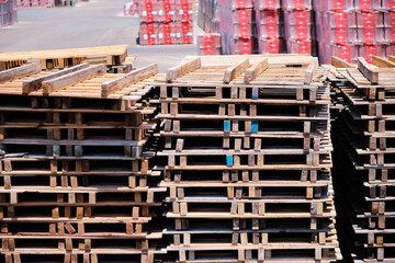 Wooden pallets stacked on a forecourt outside a factory. - obrazy, fototapety, plakaty