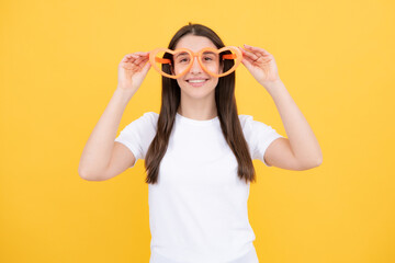 Girl with heart shaped glasses funny and smiling on yellow studio background.