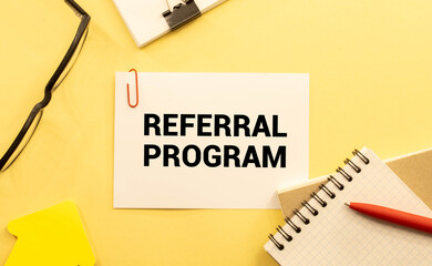 Referral Program open notepad on desktop near white keyboard and yellow stickers and glasses