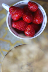 Porcelain cup filled with fresh strawberries, golden vase with gypsophila flowers and vintage tray on the table. Flat lay.