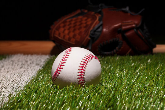 Baseball on grass field low angle close up with mitt and bat soft focus behind