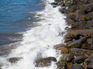 Surf. Waves crash on big rocks. Rocky coast and wave. Powerful coastline. Sea foam. The excitement of the sea.