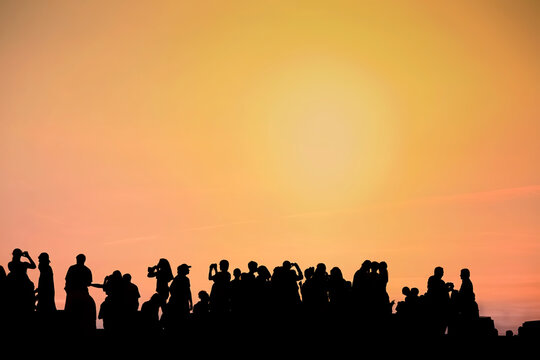 Silhouette of people taking pictures against sunset sky