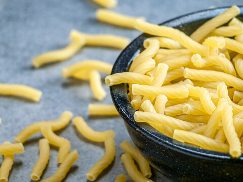 Closeup of Italian food yellow raw uncooked vermicelli, macaroni, noodle, pastry, pasta isolated dark bowl (close-up,meal, cuisine, cooking, gray, dry, dish, studio, plate, dinner, tile, cement)
